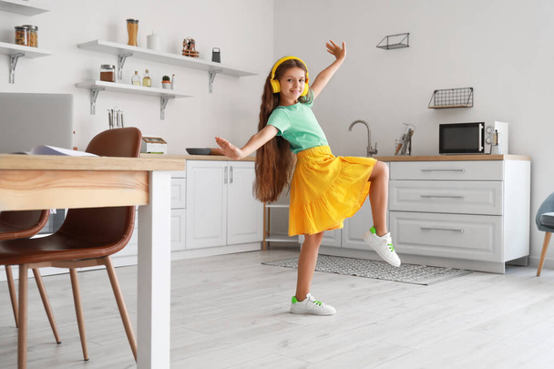 Cute little girl with yellow headphones dancing in kitchen - Foto, imagen