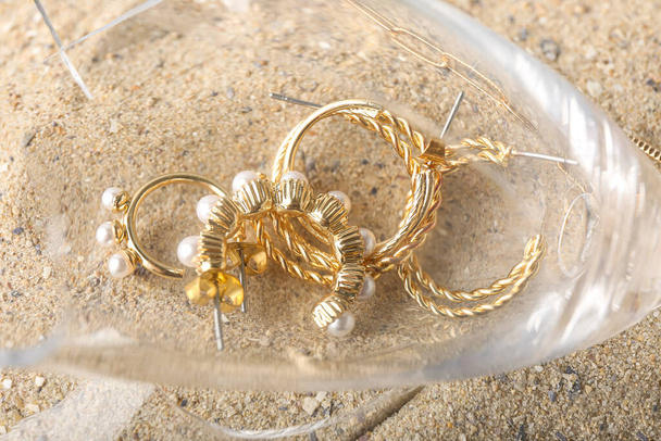 Verre cassé, bijoux dorés élégants sur sable, gros plan - Photo, image