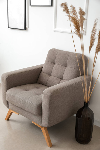 Acogedor sillón y jarrón con hierba de pampas cerca de la pared de luz - Foto, imagen