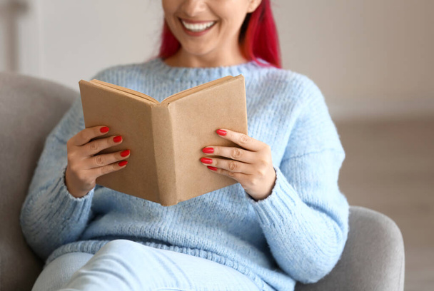 Belle femme en pull bleu livre de lecture sur canapé à la maison - Photo, image