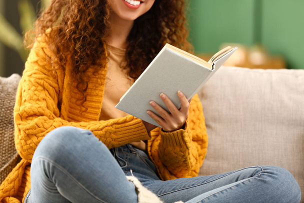 Щаслива афро-американська жінка, що читає книжку на дивані вдома. - Фото, зображення