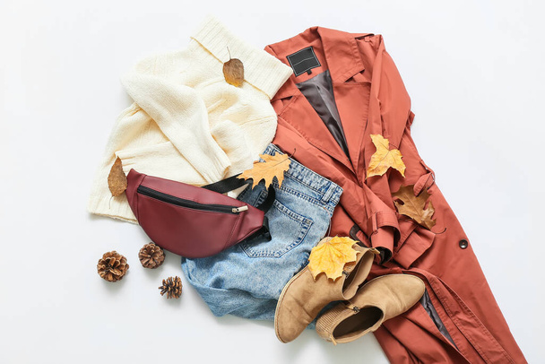 Стильне жіноче пальто, светр, джинси, сумка та осінній декор на світлому фоні
 - Фото, зображення