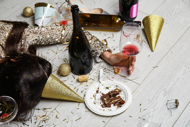 Пьяная молодая женщина с бокалом вина лежит на полу после вечеринки - Фото, изображение