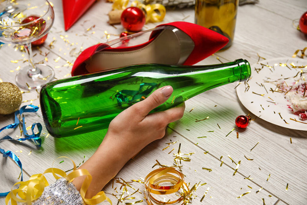 Jeune femme ivre avec une bouteille de vin vide couché sur le sol après la fête - Photo, image