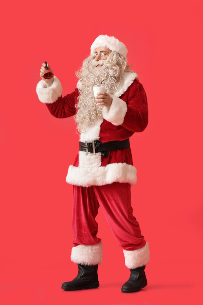 Santa Claus with glass of milk and Christmas bell on red background - Photo, image