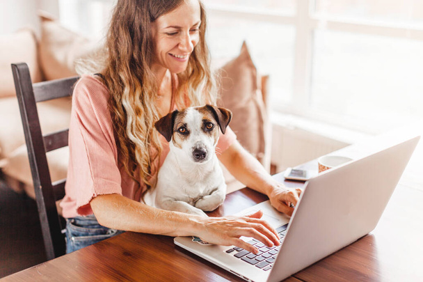 Female Hands Working On Laptop With Cute Dog. Freelancer working at home next to a puppy - Zdjęcie, obraz