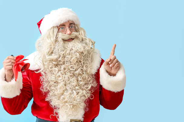 Weihnachtsmann mit Weihnachtsglocke zeigt auf etwas auf blauem Hintergrund - Foto, Bild