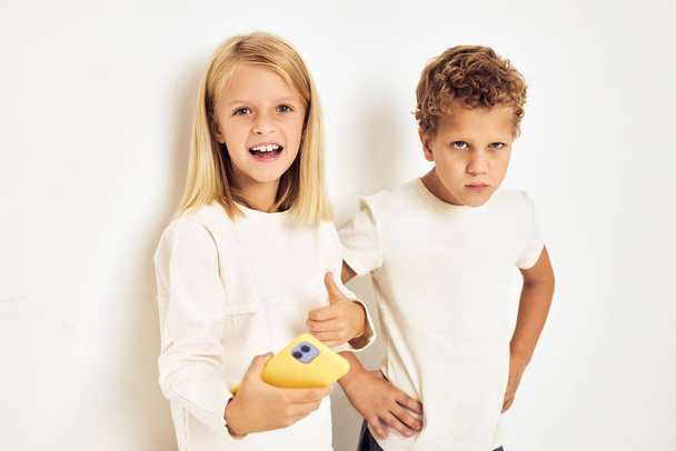 Due bambini in età prescolare ragazzo e ragazza sorridente con il telefono in mano moda luce sfondo - Foto, immagini