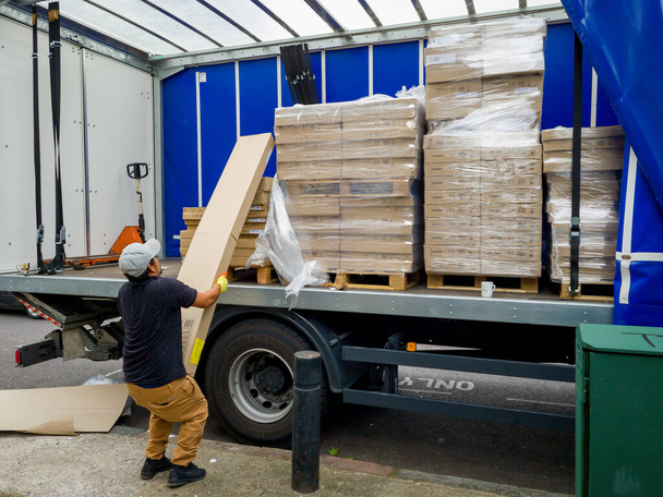 Londen. Verenigd Koninkrijk - 08.13.2021: werknemers die zware verpakkingen van een vrachtvoertuig lossen. - Foto, afbeelding
