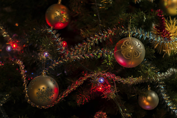 Beautiful Christmas tree decorations: balls, tinsel, a luminous garland on a dark green background. Festive mood. - Фото, изображение