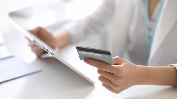 Image recadrée d'une femme d'affaires ou d'une travailleuse tenant une carte de crédit et une tablette numérique à son bureau. - Photo, image