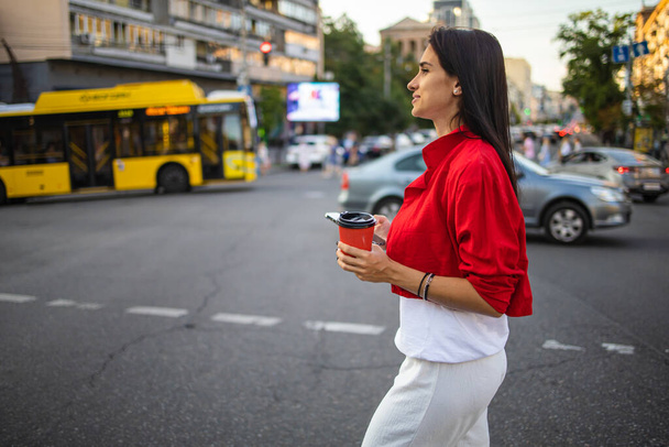 Zbliżenie żeńskie ręce trzymające smartfon i kawę na tle ulicznego przejścia. Młoda przedsiębiorczyni korzystająca z mobilnego urządzenia stojącego na drodze miejskiej - Zdjęcie, obraz