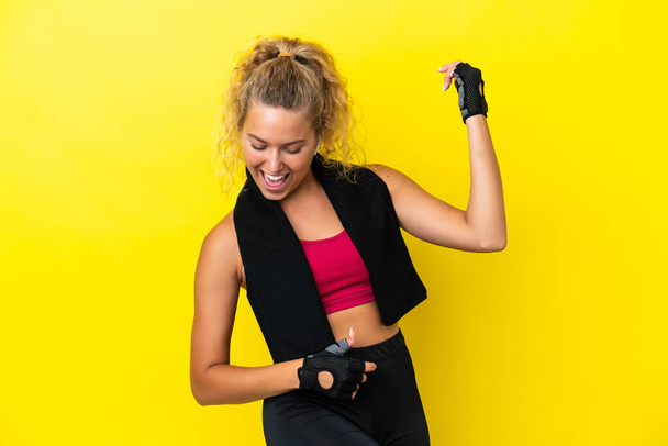 Sport woman with towel isolated on yellow background making guitar gesture - Photo, Image