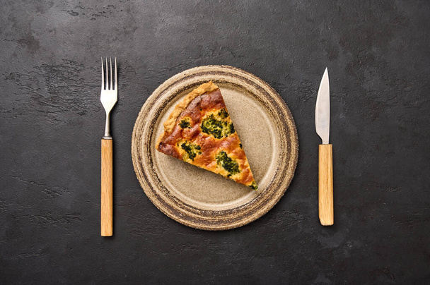 Piece of quiche tart pie on ceramic plate. Next to the knife and fork - Fotó, kép