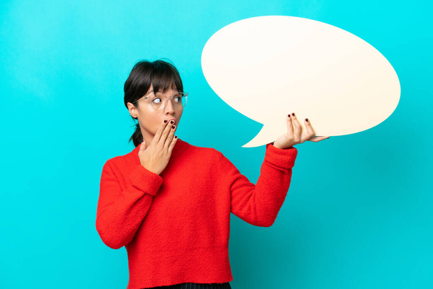 Young woman isolated on blue background holding an empty speech bubble with surprised expression - Foto, immagini