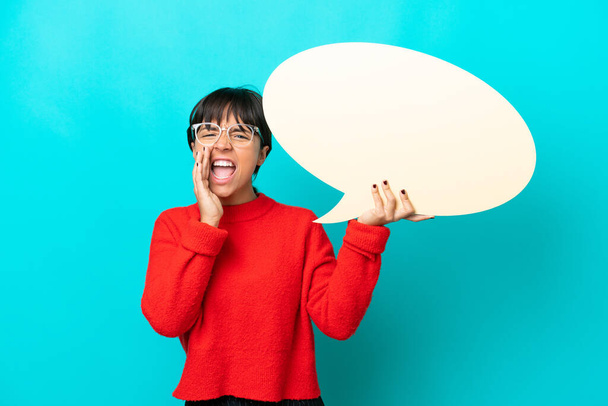 Young woman isolated on blue background holding an empty speech bubble and shouting - Zdjęcie, obraz