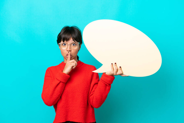 Young woman isolated on blue background holding an empty speech bubble and doing silence gesture - Photo, Image