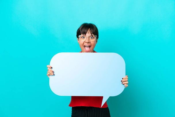 Young woman isolated on blue background holding an empty speech bubble with surprised expression - Fotoğraf, Görsel