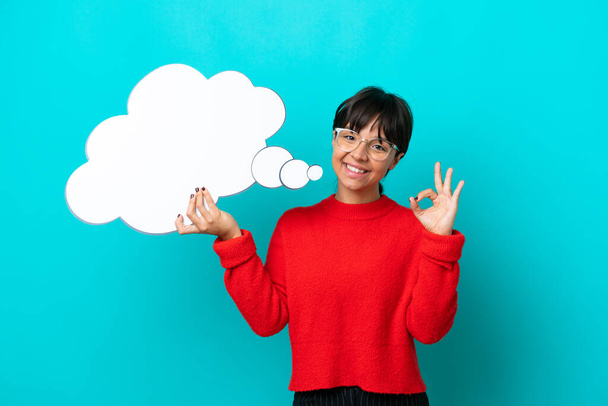 Young woman isolated on blue background holding a thinking speech bubble and doing OK sign - Photo, Image