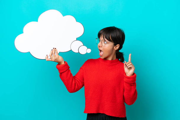Young woman isolated on blue background holding a thinking speech bubble with surprised expression - Photo, Image