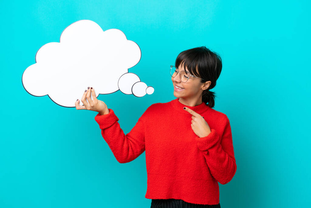 Young woman isolated on blue background holding a thinking speech bubble and pointing it - Foto, afbeelding
