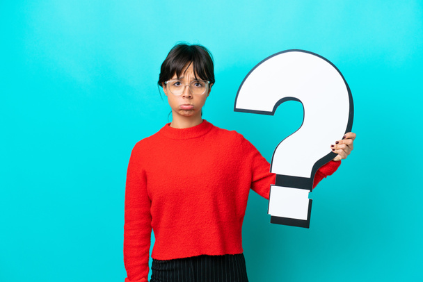Fiatal nő elszigetelt kék háttér kezében egy kérdőjel ikon és szomorú kifejezés - Fotó, kép
