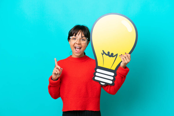 Young woman isolated on blue background holding a bulb icon and thinking - Photo, Image