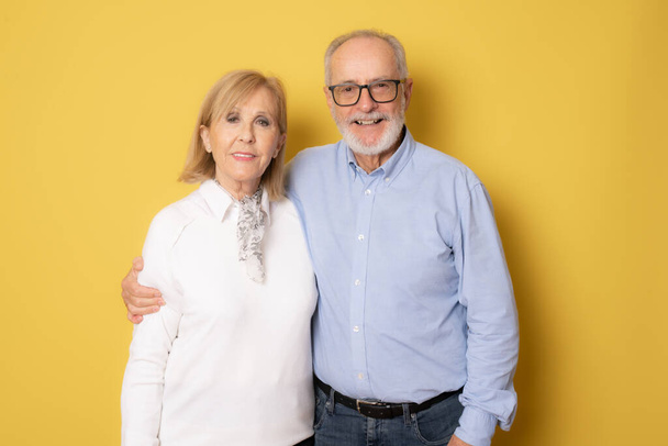 Senior smiling couple posing together over yellow background. - Photo, Image