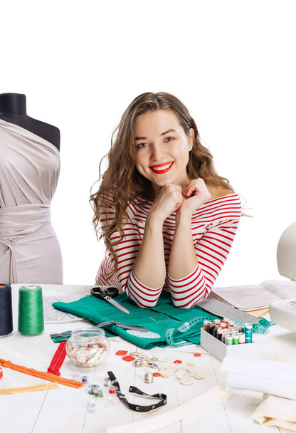 Smiling cute young girl, seamstress, dressmaker working with fabric, scissors and sewing machine isolated on white background. Concept of job, hobby - Photo, image