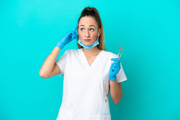 Dentist caucasian woman holding tools isolated on blue background having doubts and thinking - Fotografie, Obrázek