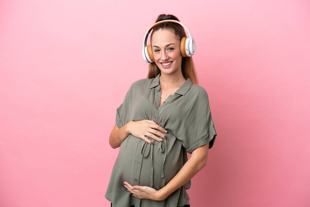 Jeune femme isolée sur fond rose enceinte et écoutant de la musique - Photo, image