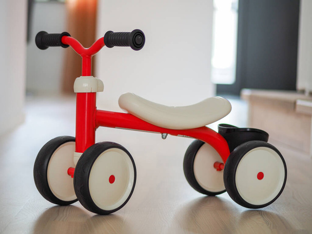 Пластиковый красный четырехколесный детский велосипед на деревянном полу - Фото, изображение