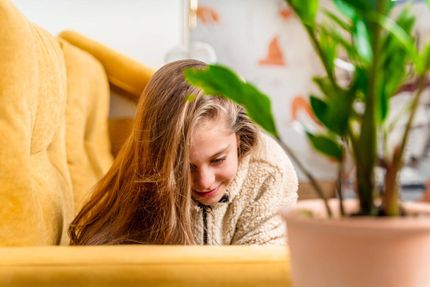 Ein schönes kleines Mädchen im Teenageralter liegt auf einem gelben Sofa und spielt mit einem Mobiltelefon oder kommuniziert mit Freunden, selektiver Fokus - Foto, Bild