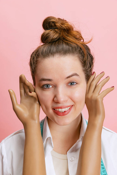 Close-up portrait of smiling girl, seamstress tailor holding mannequins plastic hands isolated on pink background. Concept of job, hobby - Foto, Bild