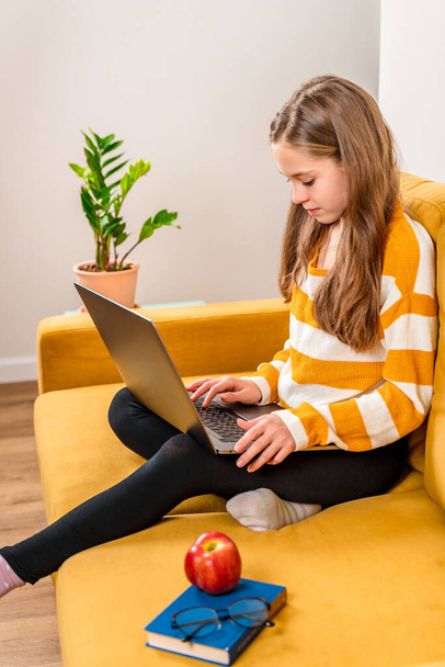 Ein lächelndes europäisches Teenager-Mädchen benutzt einen Laptop für Videoanrufe zu Freunden und Eltern, die auf einem gelben Sofa sitzen. Online-Fernunterricht. - Foto, Bild