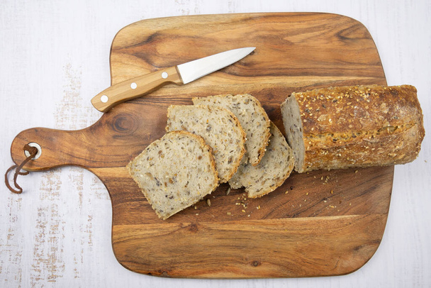 sliced homemade bread with seeds and knife on wooden board - Photo, Image