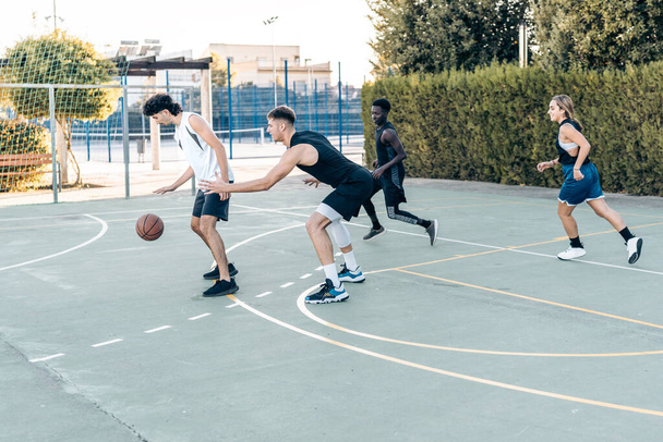 Four friends playing basketball in an urban outdoor court during sunset - Foto, imagen