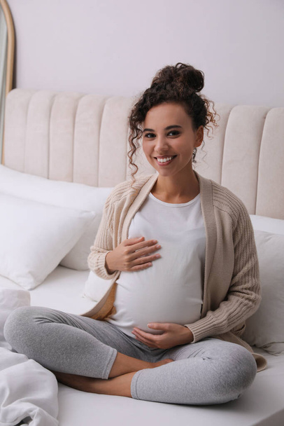 Pregnant young African-American woman sitting on bed at home - Photo, image