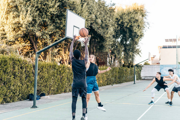 Four friends playing basketball in a public outdoor court - Fotoğraf, Görsel