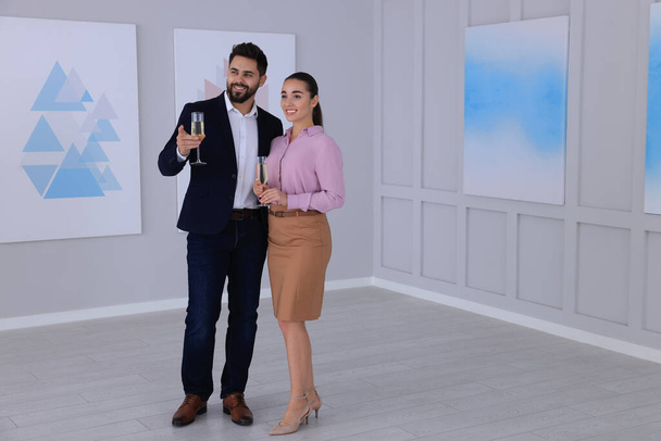 Young couple with glasses of champagne at exhibition in art gallery - Foto, Imagen