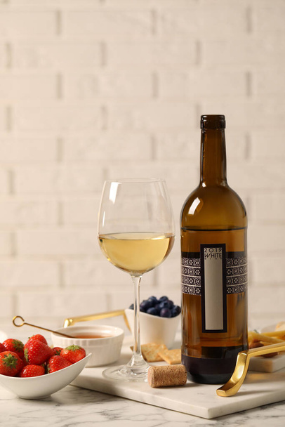 Fles wijn, glas en heerlijke snacks op witte marmeren tafel - Foto, afbeelding