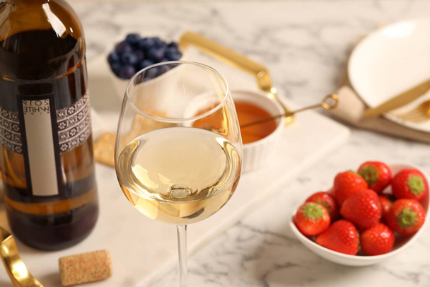 Glass of wine near bottle and delicious snacks on white table, closeup - Photo, image