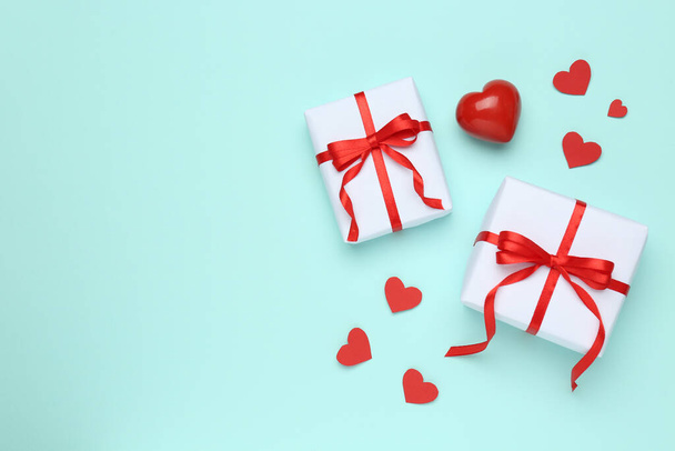 Gift boxes with decorative red hearts on turquoise background, flat lay. Space for text - 写真・画像