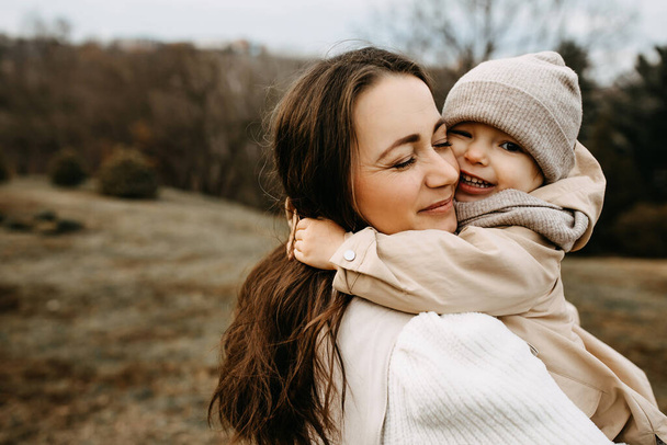 Mother holding little daughter in arms, hugging, outdoors, in a park, on autumn day. - Foto, Imagen