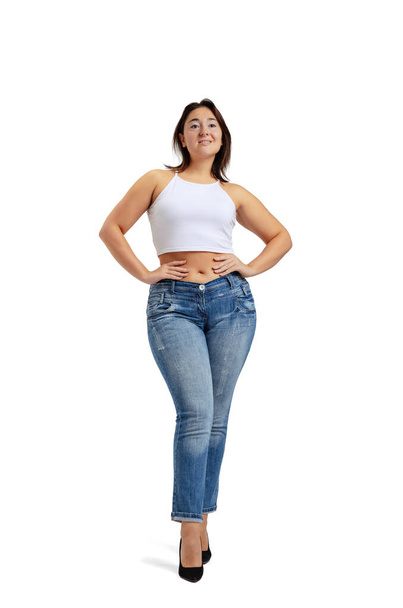 Full-length portrait of plus-size woman wearing white t-shirt and jeans posing isolated on white studio background. Body positive concept - Foto, Bild