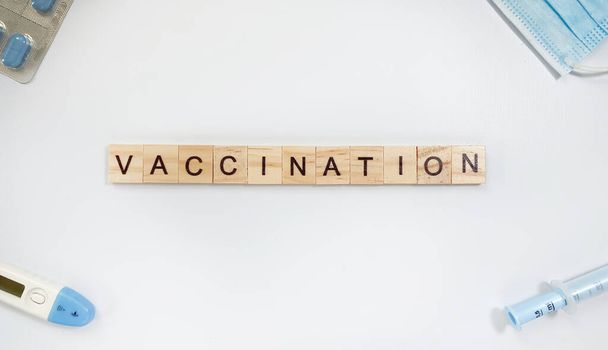 Layout mit dem Wort Impfung aus Holzbuchstaben und in der Nähe einer Spritze, Thermometer, Medikamentenmaske und Pillen - Foto, Bild