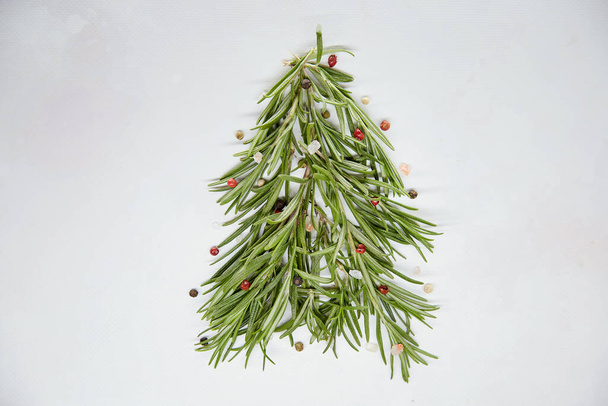Feestelijke creatieve kerstboom gemaakt met rozemarijn en versierd met peperkorrels en zeezout. Seizoensgebonden stijl. Groen achtergrond. Kopieer ruimte.. - Foto, afbeelding