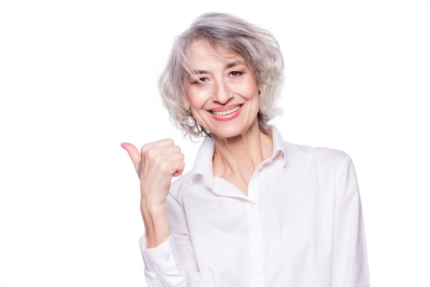 Close up portrait of a happy smiling mature woman in her sixties with trendy grey hair making thumbs up hand sign expressing approval isolated on white background - Zdjęcie, obraz