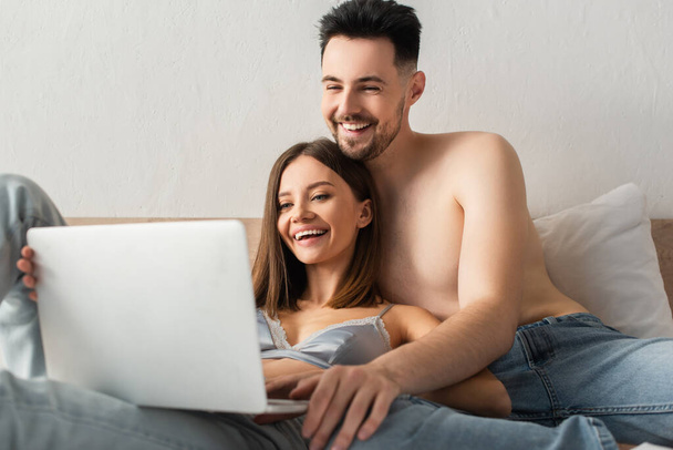joyful couple of lovers watching comedy film on blurred laptop in bed - Fotó, kép