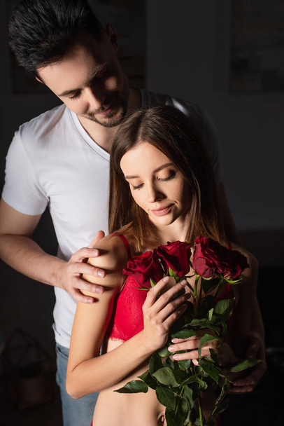 man in white t-shirt smiling near young sexy woman with red roses - Фото, изображение